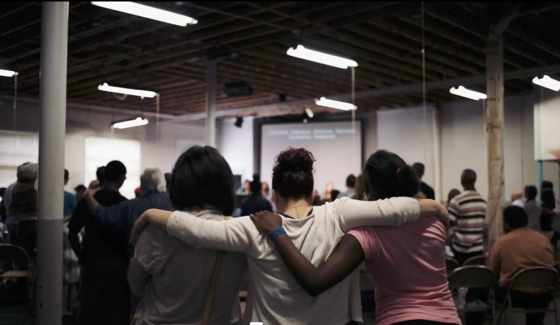 A small group of pople linking arms and in prayer.